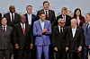 Pedro Sánchez står midt i en gruppe smilende konferansedeltakere på et podium.