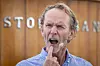 Harald Magnus Andreassen taler på scene med mikrofon, foran en trevegg med synlig Sparebank 1-logo.
