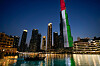 Turistbåt på vannet foran Dubai-fontenen og Burj Khalifa opplyst i UAE-fargene.