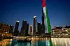 Turistbåt på vannet foran Dubai-fontenen og Burj Khalifa opplyst i UAE-fargene.