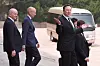 Elon Musk går ut fra en velkomstseremoni i Beijing mens sikkerhetsfolk og en minibuss er i bakgrunnen.