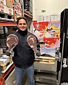 Mann i butikklager holder to store kjøttstykker foran hyller og esker.