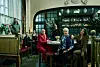 Flere personer sitter rundt et bord i en bar med mørke møbler og flasker i bakgrunnen.