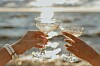 To hender skåler med champagneglass foran glitrende vann.