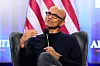 Satya Nadella holder en mikrofon og taler foran et amerikansk flagg på USA House i Davos.