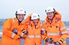 Tre statsråder i oransje arbeidstøy og hjelmer står sammen utendørs ved Aibel i Haugesund.