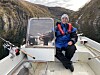 Person sitter i liten båt med fiskestenger i et smalt fjordområde omgitt av bratte fjell.