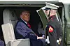 President Donald Trump sitter i en helikopterdør mens en marinesoldat står ved siden av under ombordstigning i Marine One.