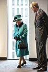 Dronning Elizabeth II i grønn kåpe og hatt går innendørs ved et vindu ved siden av en mann i dress.