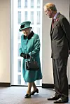 Dronning Elizabeth II i grønn kåpe og hatt går innendørs ved et vindu ved siden av en mann i dress.