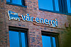 Vår Energi-logo i lys skrift på en mursteinsfasade med vinduer.