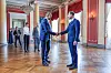 Kronprins Haakon håndhilser i en stor sal på Det kongelige slott, med røde vegger og høye vinduer.