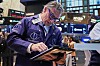 Trader John Romolo ser ned på en nettbrett på gulvet i New York Stock Exchange med skjermer og logoer i bakgrunnen.