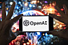 Mobil med OpenAI-logo foran et fargerikt, uskarpt bilde i bakgrunnen.