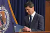 Kevin Warsh står ved en talerstol og ser ned på notater foran et Federal Reserve-flagg.