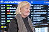 Gro Bakstad foran en digital avgangstavle på en jernbanestasjon i Oslo