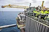 Arbeidere i verneutstyr på Valhall-plattformen over Nordsjøen, med kraner og hav i bakgrunnen.