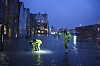 Oversvømt gate på Bryggen i Bergen med to personer i refleksklær i vannet.