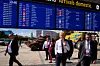 Reisende går utenfor en flyterminal under en digital tavle for innenriksankomster.