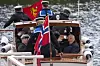 Kong Harald vinker fra en båt i Samnanger, med det norske flagget i forgrunnen.