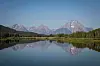 Teton-fjellene og grønne skoger speiler seg i det stille vannet ved Oxbow Bend.