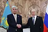 Vladimir Putin og Kassym-Zjomart Tokajev håndhilser foran Kasakhstans og Russlands flagg.