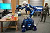 Humanoid robot strekker seg mot en pakke kjeks på et bord under en robotikkdemonstrasjon i Brussel.