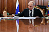 Vladimir Putin sitter ved et blankpolert bord i et trepanelkledd rom med Russlands flagg bak seg.
