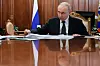 Vladimir Putin sitter ved et blankpolert bord i et trepanelkledd rom med Russlands flagg bak seg.