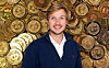 Smilende mann i mørk genser foran en bakgrunn med Bitcoin-mynter.