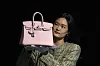 En ansatt viser fram en rosa Hermès Birkin-veske foran en svart bakgrunn.